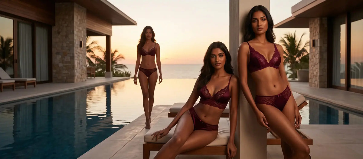 Three women in burgundy bikinis posing by a pool with a sunset view.